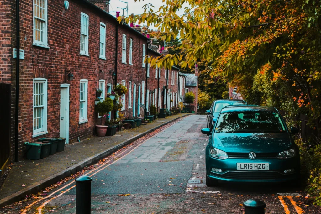 Cars parked beside the road near trees and buildings on a UK residential street