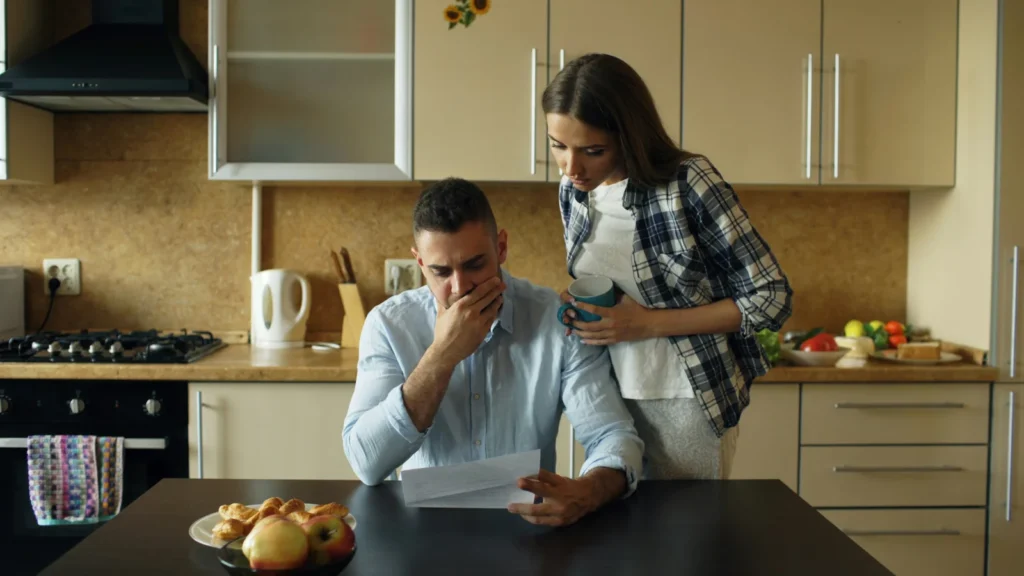 Couple looking stressed over bills at a kitchen table before speaking to a mortgage renewal adviser
